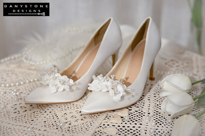 Top view of Elegant White Silk Satin Wedding Heels with floral and pearl design on a lace tablecloth.