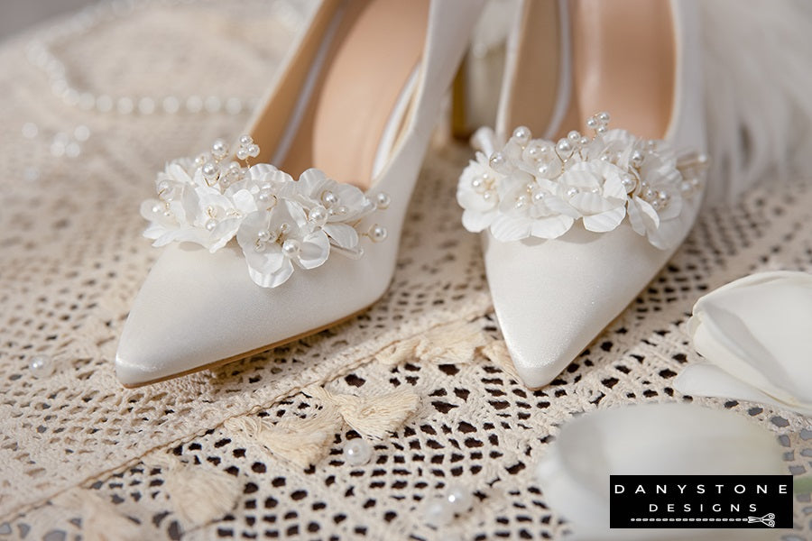 Side view of Elegant White Silk Satin Wedding Heels with floral embellishments, displayed on a lace tablecloth.