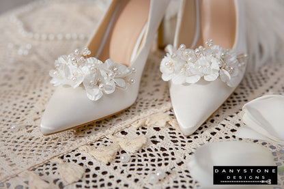 Side view of Elegant White Silk Satin Wedding Heels with floral embellishments, displayed on a lace tablecloth.