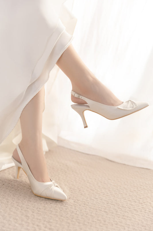 White high-heeled shoes worn with a white dress on a neutral background