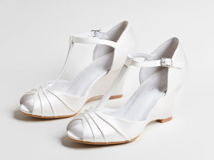 Pair of white wedding shoes with open toes and thin straps on a light gray background