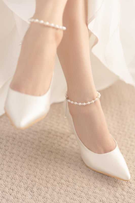 White wedding shoes with pearl anklets on a neutral background