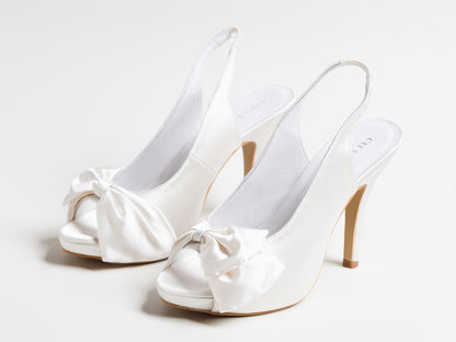 White wedding shoes with bow details on a light gray background