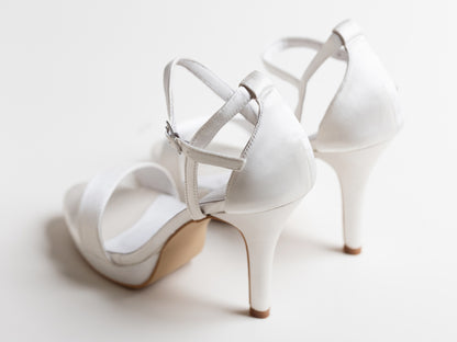 White high-heeled shoes with thin straps on a light background