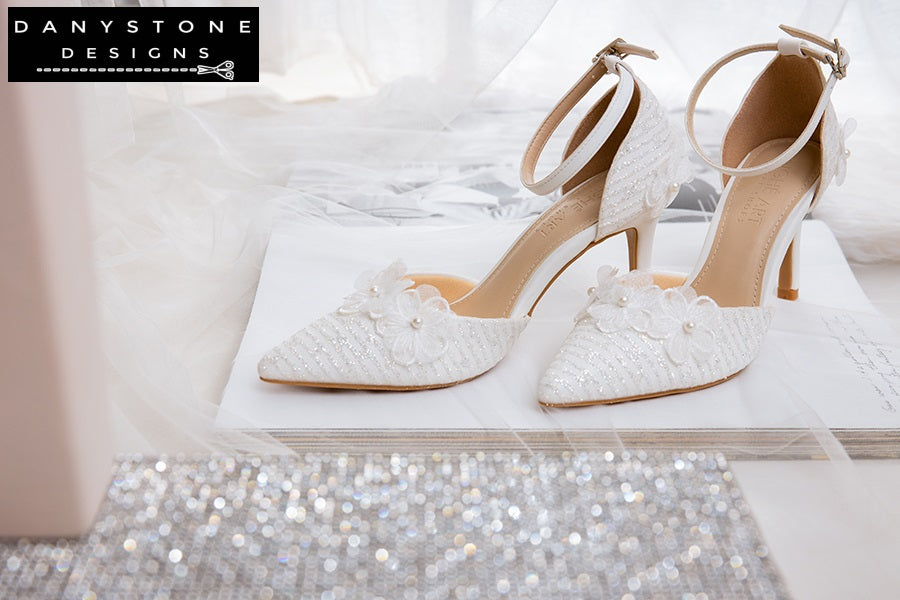 Rear view of white lace wedding shoes with floral details and ankle straps, displayed on a soft, furry surface.