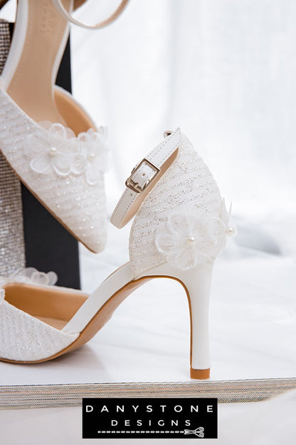 Top view of white lace bridal shoes with floral decorations and 9cm heel, arranged on an open book.