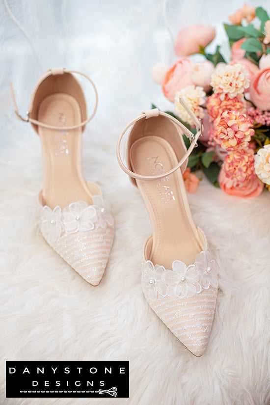 Close-up of white lace bridal shoes with ankle strap, 9cm heel, decorated with flowers and metallic lace.