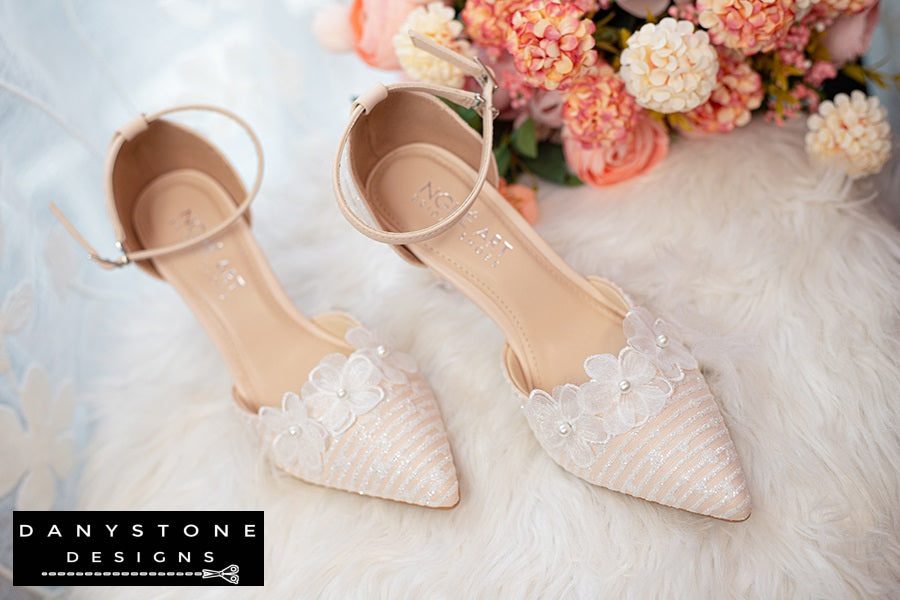 Close-up of white lace bridal shoes with ankle strap, 9cm heel, decorated with flowers and metallic lace.