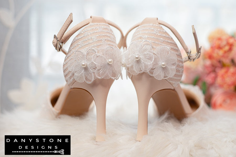 Back view of white lace bridal heels with floral details and ankle strap, showcased on a glittery box.