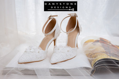 Back view of white lace bridal heels with floral details and ankle strap, showcased on a glittery box.