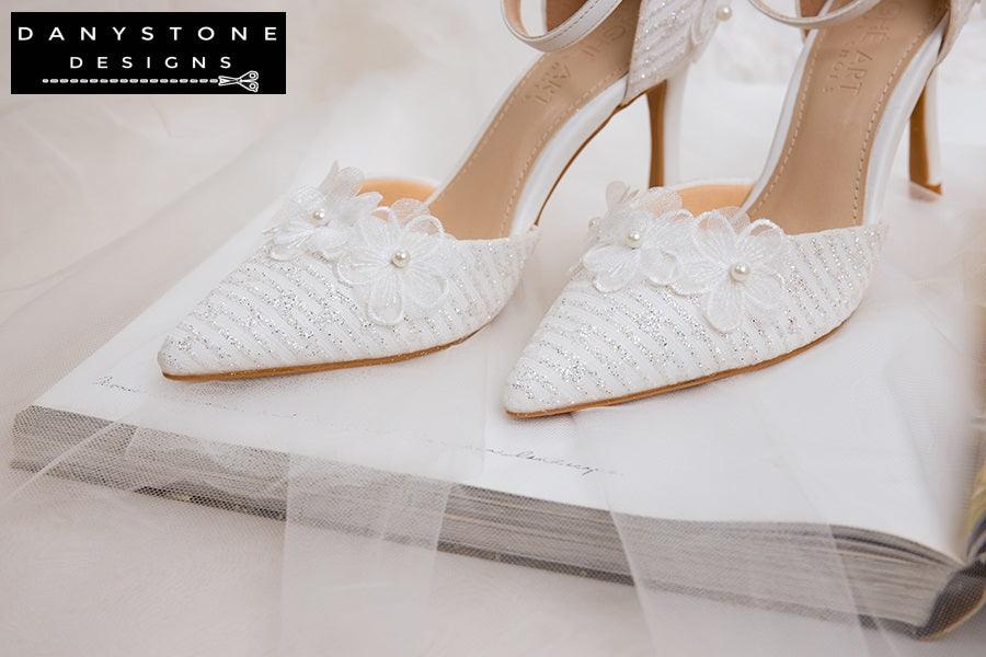 Pair of white lace wedding shoes with floral decorations, 9cm heel, displayed on a soft, furry surface.