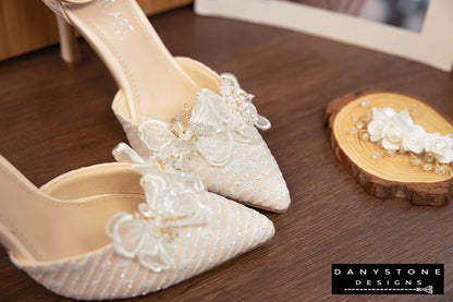 White bridal shoes with chiffon butterfly wings and 9cm heels, displayed on a soft white surface with tulips in the background.