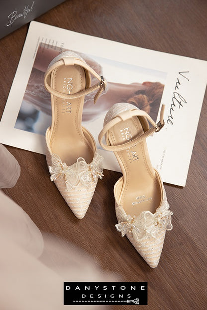 White bridal shoes with chiffon butterfly wings and 9cm heels, displayed on a soft white surface with tulips in the background.