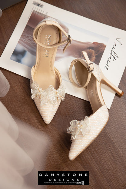 Nude bridal shoes with metallic lace fabric and chiffon butterfly wings, showcased on a wooden surface.