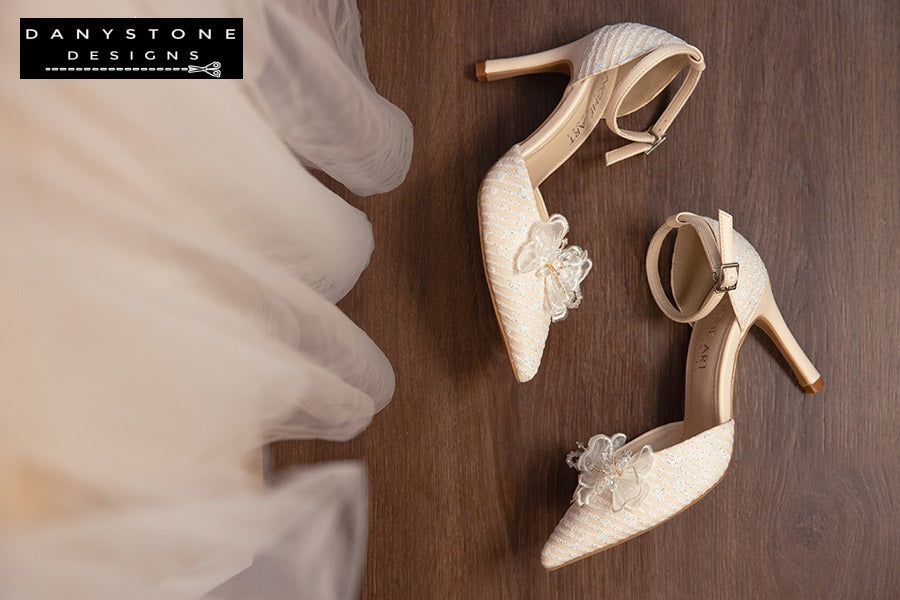 Nude bridal shoes with metallic lace fabric and chiffon butterfly wings, showcased on a wooden surface.