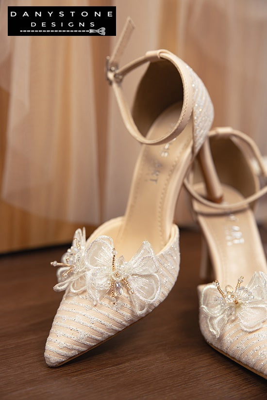 Close-up of bridal shoes with chiffon butterfly wings and metallic lace fabric, highlighting intricate details.