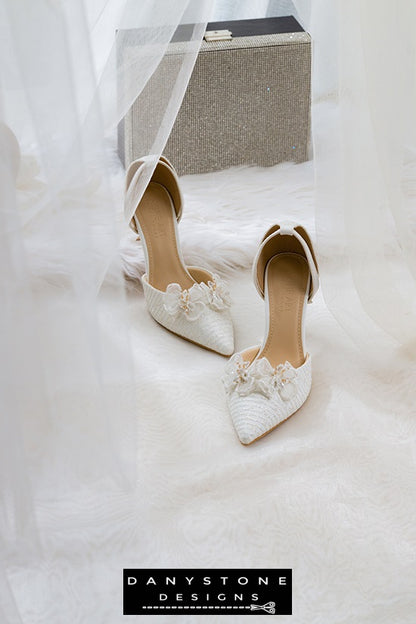 White bridal shoes with chiffon butterfly wings and 9cm heels, displayed on a white surface with a bridal bag and flowers in the background.