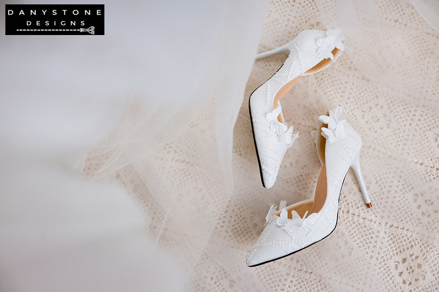 Close-up of the front view of white lace wedding shoes with butterfly decor, showcasing the intricate lace and butterfly details.