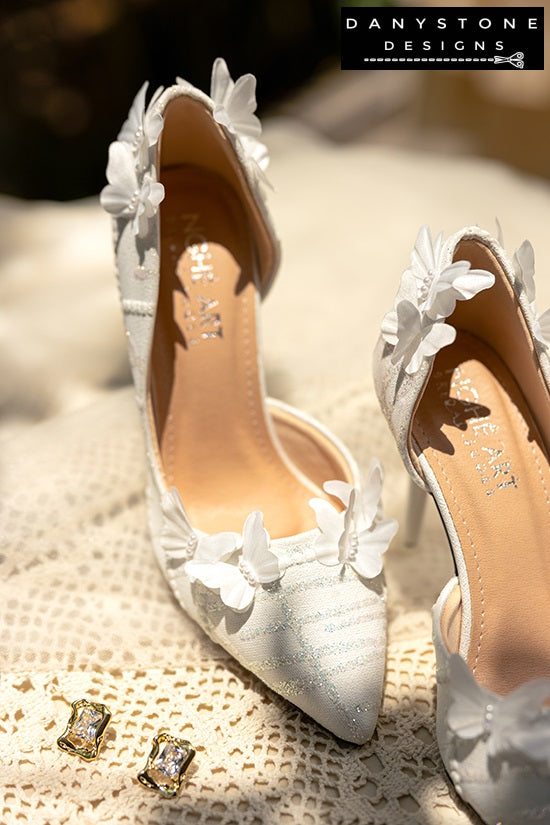 White lace wedding shoes with butterfly decor and 9cm heels, placed on a lacy fabric surface with sunlight highlighting the details.