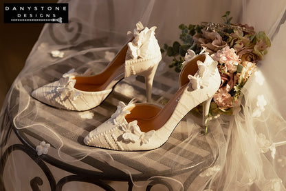 Side view of white lace wedding shoes with butterfly decor and 9cm heels, displayed with a glittery box and a sheer fabric backdrop.