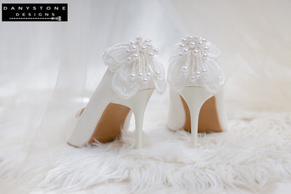 Side view of white wedding shoes with butterfly wings, set against a floral background.