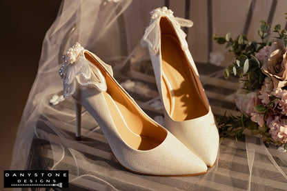 Pair of white wedding shoes with butterfly wings, shown in a romantic setting with flowers and tulle.