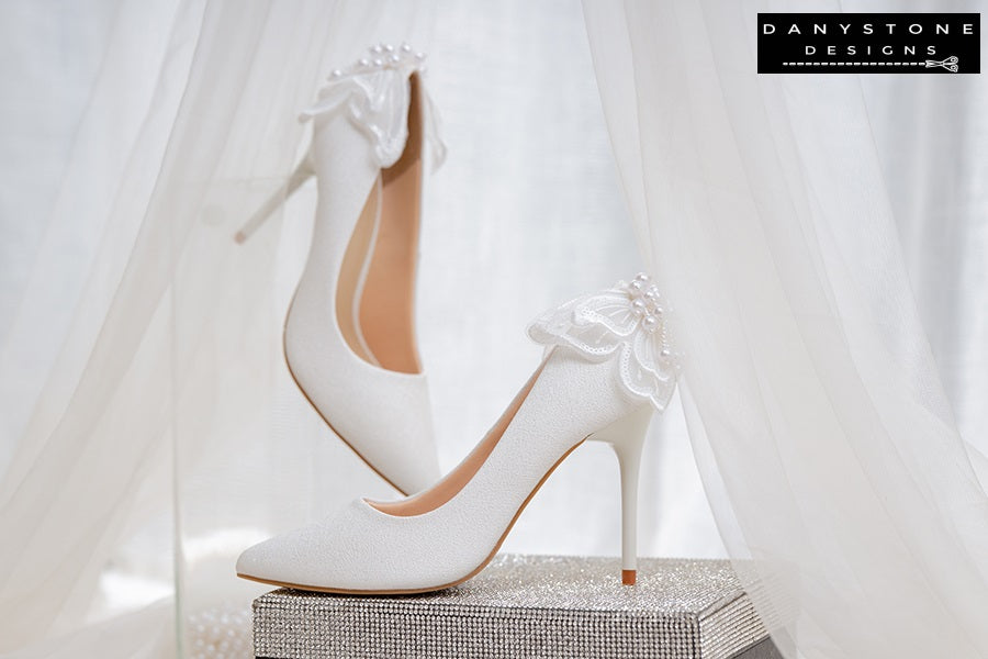 White wedding shoes with butterfly wings, elegantly displayed on a glittery box with a sheer fabric backdrop.