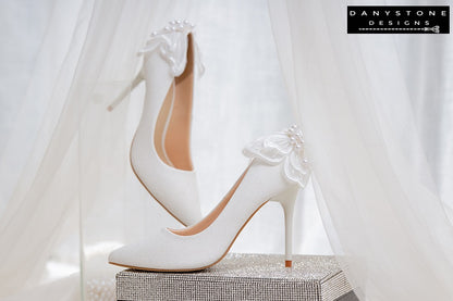 White wedding shoes with butterfly wings, elegantly displayed on a glittery box with a sheer fabric backdrop.