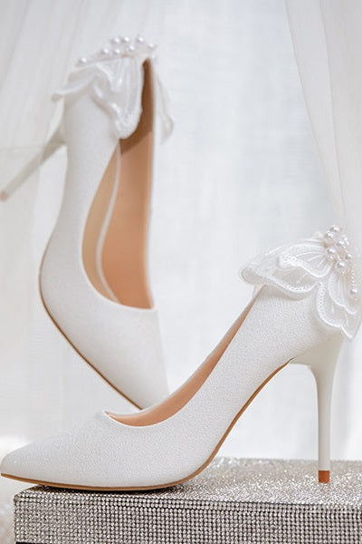 White wedding shoes with butterfly wings, elegantly displayed on a glittery box with a sheer fabric backdrop.