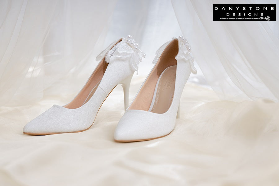 Close-up of white wedding shoes with butterfly wings, displayed on a soft, fluffy surface.