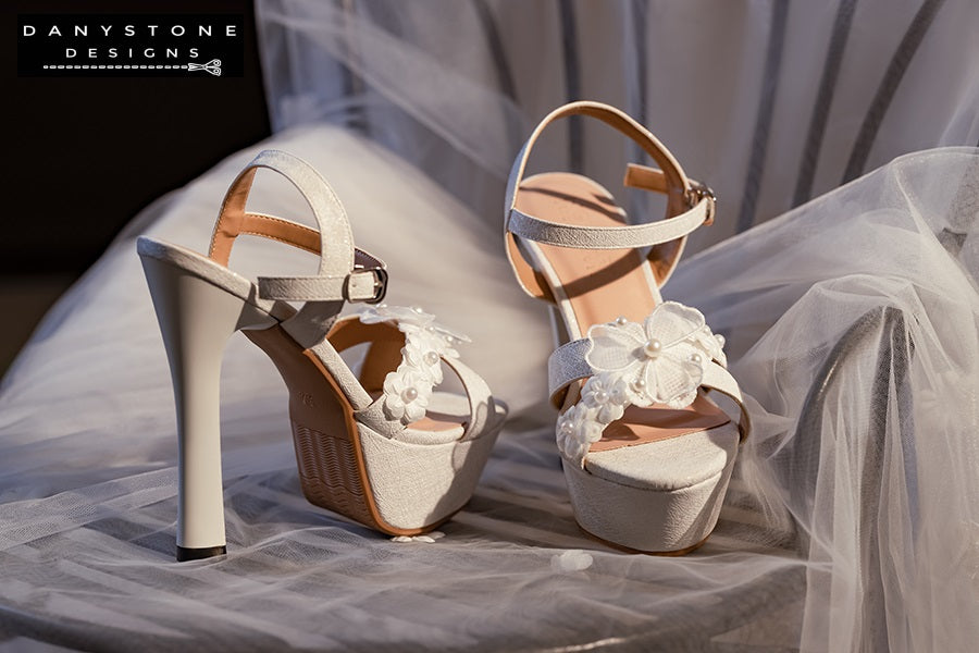 Elegant White Floral Wedding High Heels on a wooden surface with rolled-up white fabric in the background.