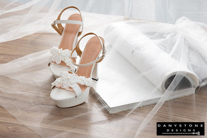 Elegant White Floral Wedding High Heels on a wooden surface with tulle and white fabric background.