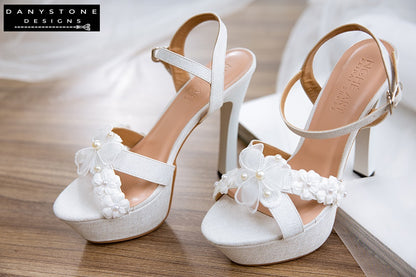 Elegant White Floral Wedding High Heels on a wooden surface with tulle and white fabric background.