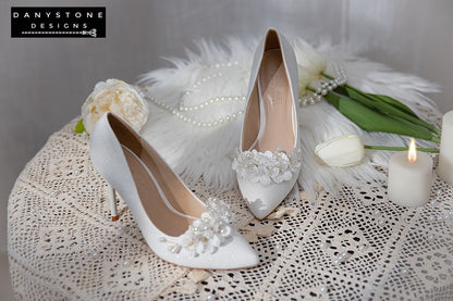 Top view of Elegant White Metallic Leather Wedding Heels with hand-woven floral and pearl design on a lace tablecloth.