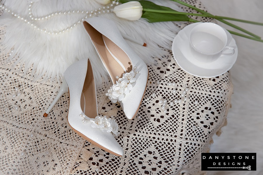 Side view of Elegant White Metallic Leather Wedding Heels with floral embellishments, displayed with a white flower and candle.