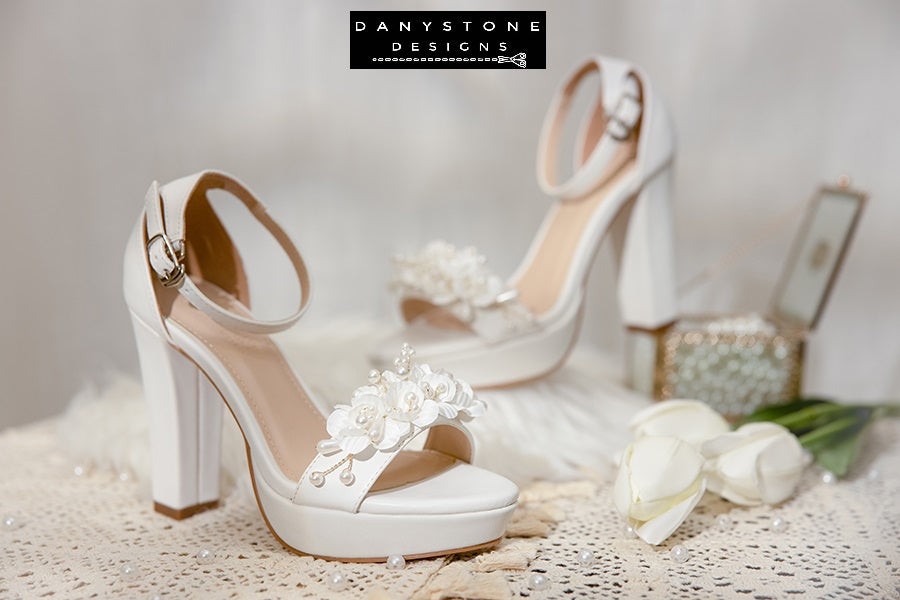 Top view of Elegant White Matte Leather Wedding Sandals with floral and pearl design on a lace tablecloth.