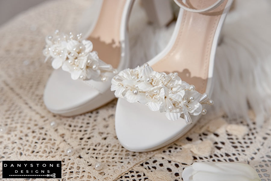 Elegant White Matte Leather Wedding Sandals with pearl flowers on a lace tablecloth.