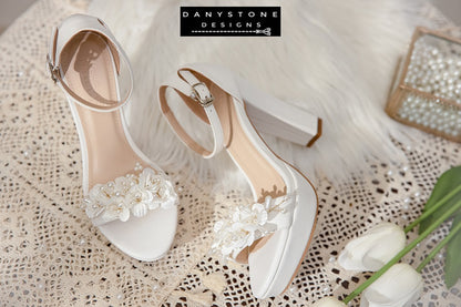 Side view of Elegant White Matte Leather Wedding Sandals with pearl flowers, displayed with white tulips and a decorative box.