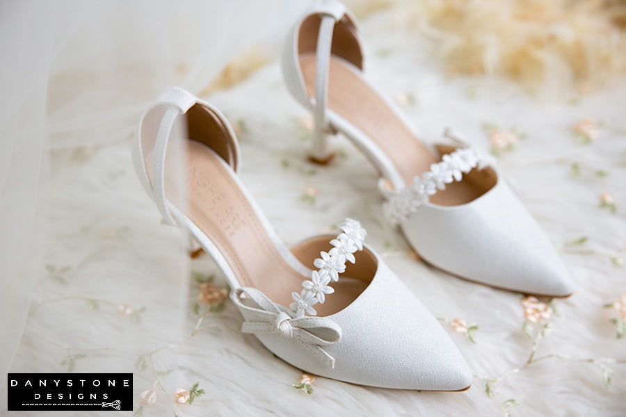 White bridal shoes featuring floral straps and bows, 7cm heels, made from metallic scratched leather for a luxurious look.