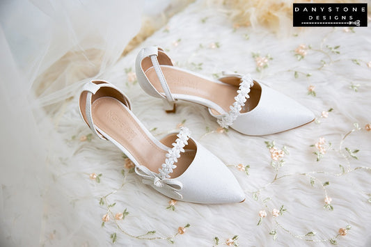 Elegant white bridal shoes with floral straps and bows, featuring a 7cm heel, made from metallic scratched leather.