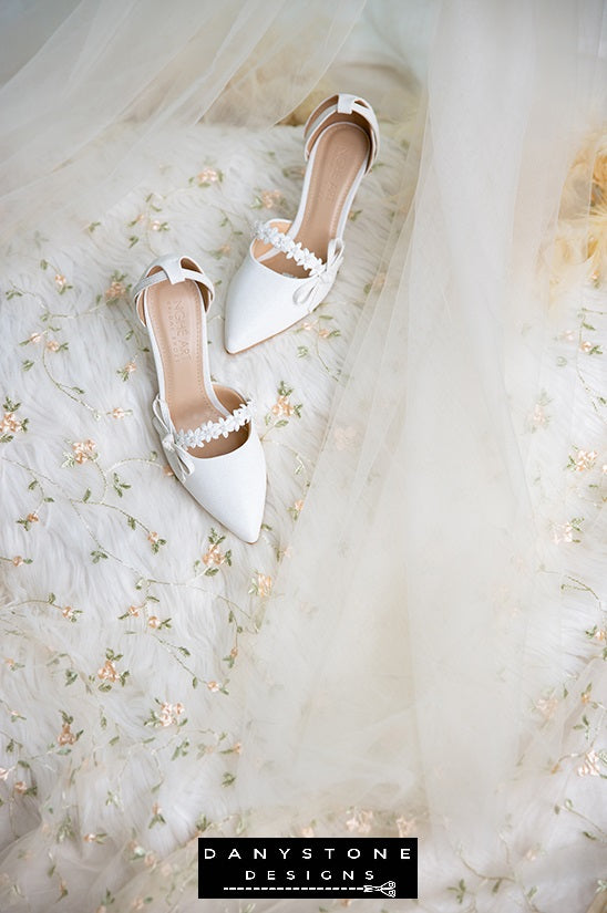 Pair of white bridal shoes with 7cm heels, showcasing floral straps and bows, perfect for a sophisticated wedding look.