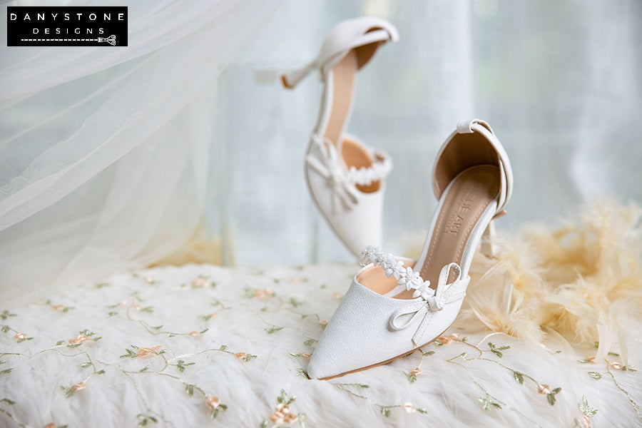 Close-up of white bridal shoes with floral straps and delicate bows, 7cm heels, made from metallic scratched leather.