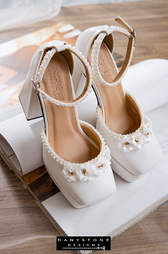 Top view of white high heels with double square toe, pearl trim, and floral accents, made from matte white leather.