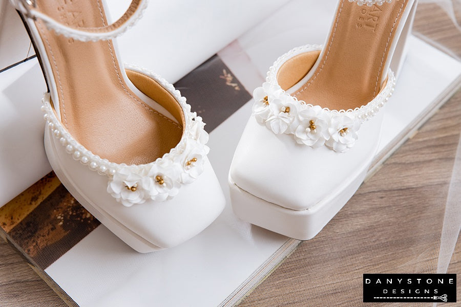 Close-up of white wedding heels with double square toe, pearl strings, and floral decorations, 13cm heel.