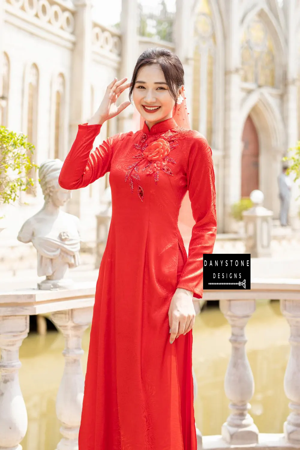 Woman in a red brocade bridal Áo Dài with large floral embellishments, smiling.