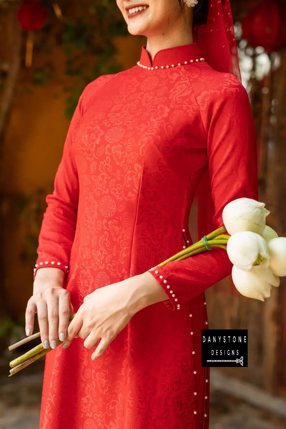 Red brocade Áo Dài with 4 panels and floral design, worn by a bride in a graceful pose.