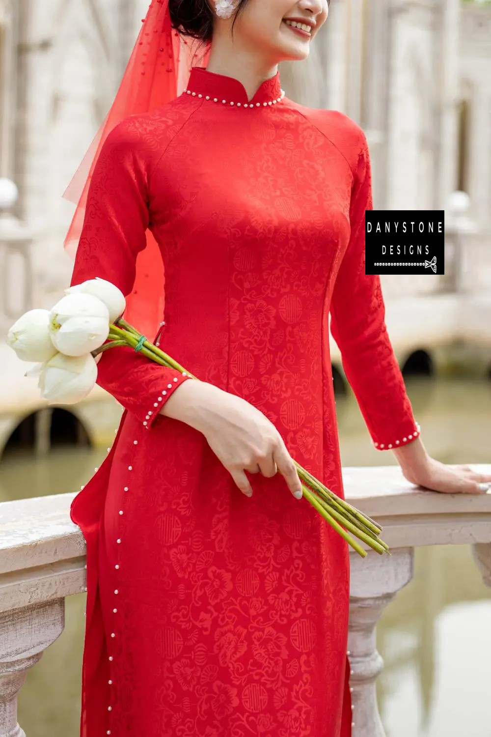 Full-length view of a bride in a red brocade Áo Dài with 4 panels, standing in an elegant setting.