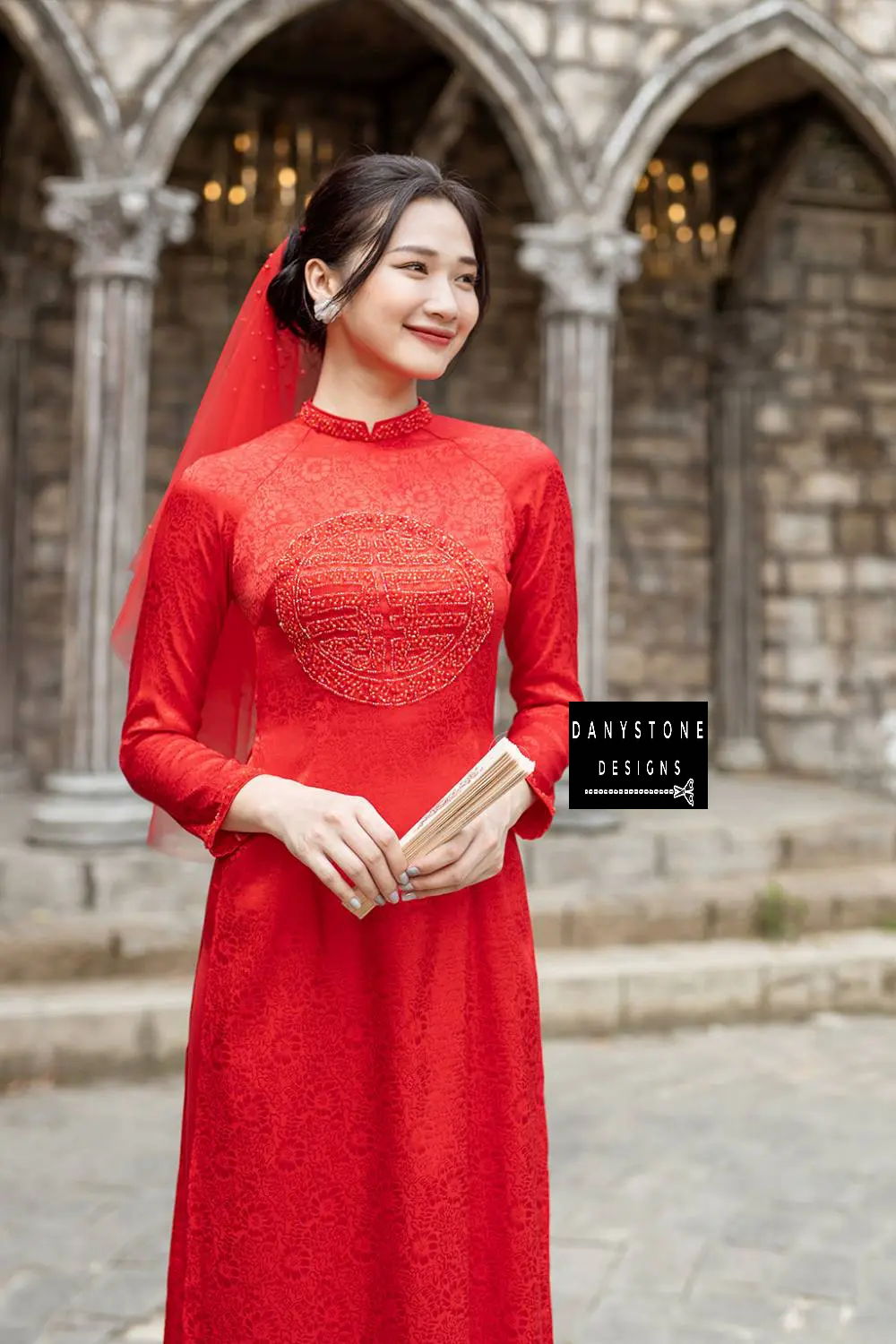 Full-length view of a bride wearing the Red Brocade Bridal Ao Dai with intricate patterns and vibrant crimson color.