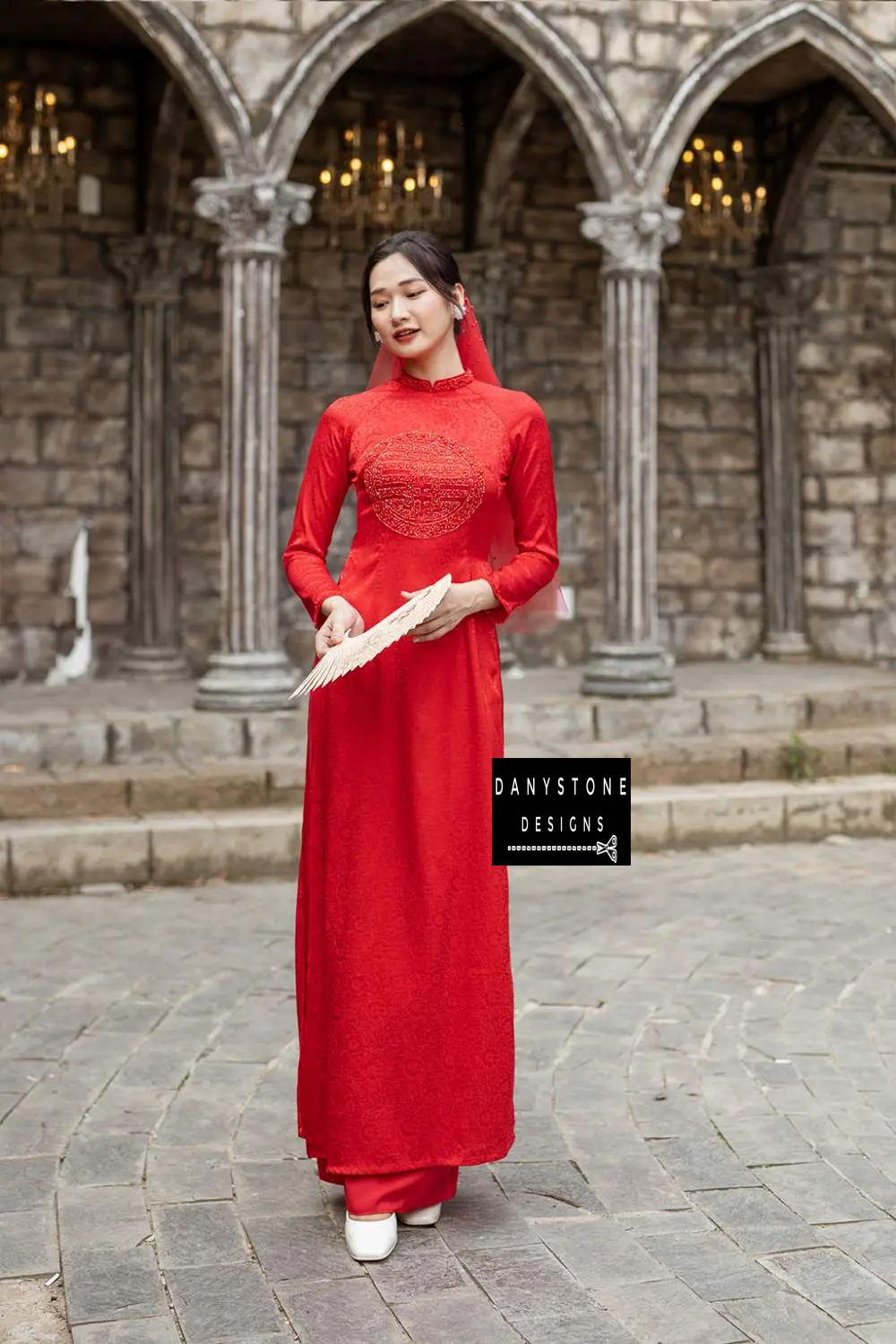 Bride holding a fan in the Red Brocade Bridal Ao Dai, capturing the traditional and charming essence of the dress.