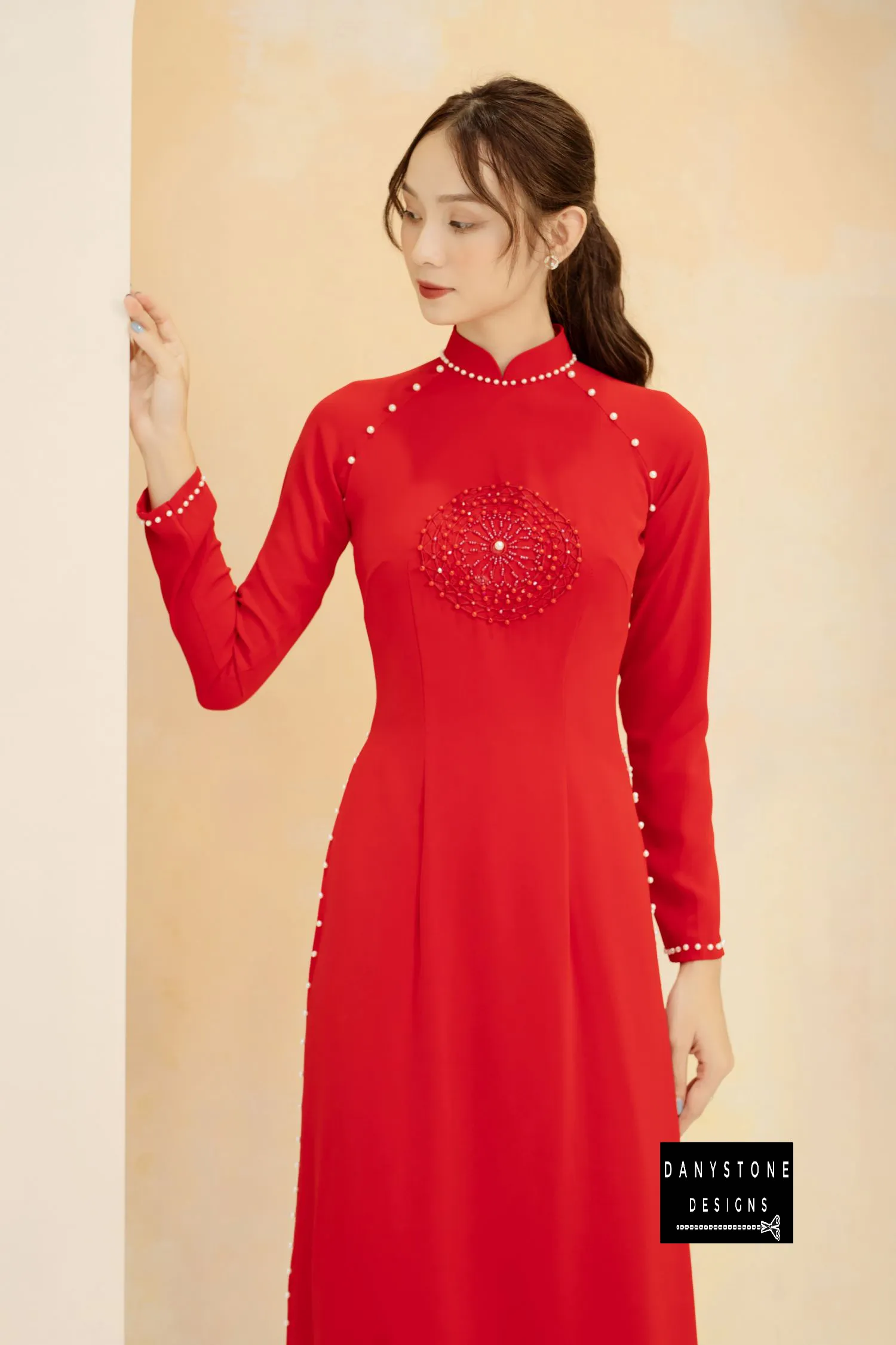 Full-length view of a bride in a red silk Áo Dài, highlighting the pearl details on the sleeves.